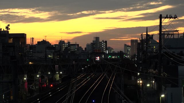 TOKYO, JAPAN - JUL 2025 : Sunset over a railway in a Tokyo residential area. A train arriving at the station during the golden hour, showcasing the daily commuter life. Time lapse shot, dusk to night.