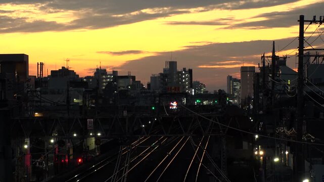 TOKYO, JAPAN - JUL 2025 : Sunset over a railway in a Tokyo residential area. A train arriving at the station during the golden hour, showcasing the daily commuter life. Time lapse shot, dusk to night.