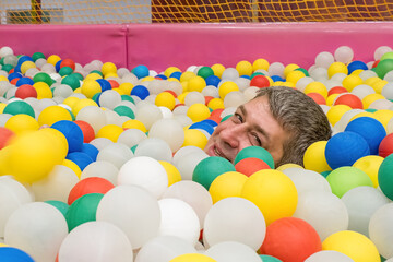 A smiling man against a background of colorful plastic balls. A festive event.