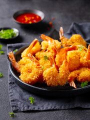 Shrimp tempura with chili sauce on a black plate. Dark grey background. Close up.
