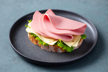 Delicious open sandwich with ham, cheese and fresh lettuce on rustic bread. Grey background. Close up. © annapustynnikova