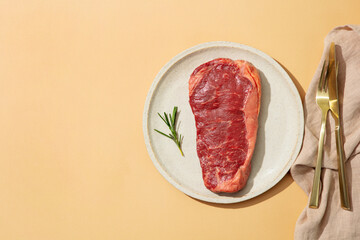 Fresh Raw Steak with Herbs on a white plate. Beige background. Copy space. Top view.