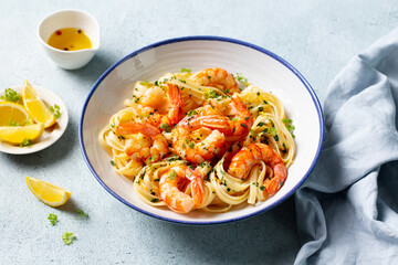 Delicious shrimp pasta dish with lemon accents and fresh herbs. Light blue background. Close up.