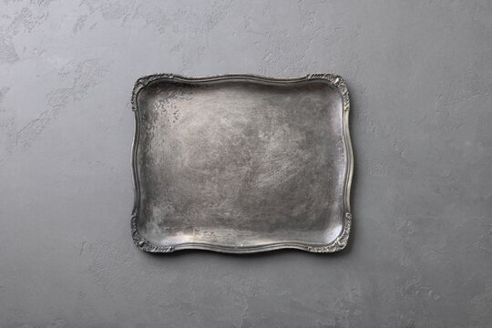 Elegant silver tray with ornate edges on textured gray background. Copy space. Top view.