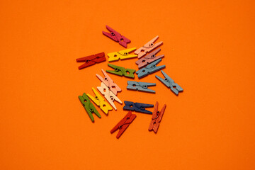 Miniature wooden clothespins arranged on a bright orange background. The small clips are neatly placed, creating a playful and creative composition