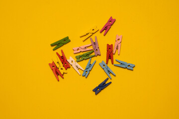 Miniature wooden clothespins arranged on a bright yellow background. The small clips are neatly placed, creating a playful and creative composition