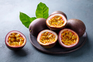 Fresh passion fruit on a black plate. A juicy tropical treat. Grey background. Close up.
