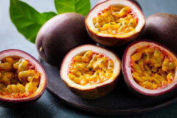 Fresh passion fruit on a black plate. A juicy tropical treat. Grey background. Close up.