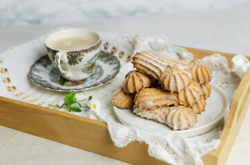 Tasty shortbread cookies with beautiful edges and powdered sugar next to a cup of coffee on a tray with a lace napkin. Coffee time concept. Selective focus. Horizontal orientation
