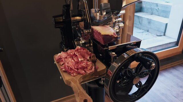 Vintage flywheel meat slicer cuts cured ham into thin slices on board, close-up in deli or restaurant