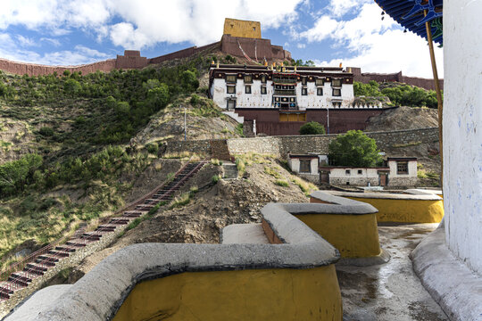 View of ancient fortress walls crown the hill, overlooking traditional Tibetan architecture nestled amidst rugged terrain under a vast sky, Gyatse, China.