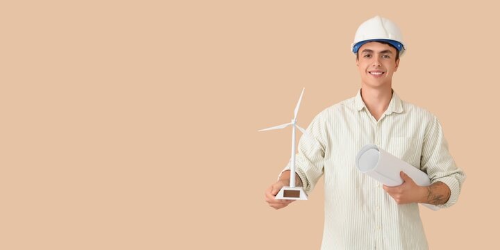 Male engineer with wind turbine model and drawing on beige background with space for text