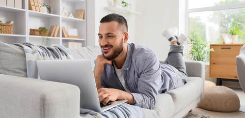 Young man using laptop while lying on sofa at home