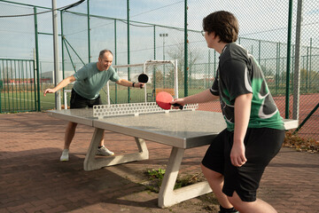 dwie osoby grające w tenisa stołowego na zewnątrz, na obiekcie sportowym © siwyk