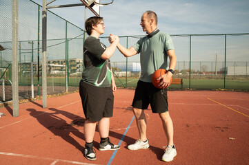 dwóch mężczyzn gratulujących sobie po zakończonej rywalizacji w koszykówkę na zewnętrznym boisku do kosza w słoneczny dzień. © siwyk