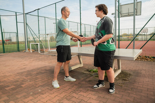 dwóch mężczyzn podająca sobie dłonie po zakończonej rywalizacji w tenisa stołowego na zewnątrz obiektu sportowego