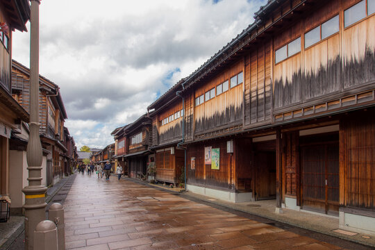 View of aged wooden buildings line a wet stone street under a cloudy sky, evoking a sense of historical preservation and quiet charm, Kanazawa, Ishikawa, Japan.