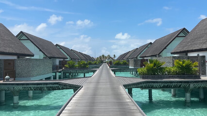 Luxury resort photo of Maldives tropical paradise island in Indian Ocean with overwater thatched bungalows, wooden bridge. Beautiful photography, coral reef, azure ocean, sky with clouds. 