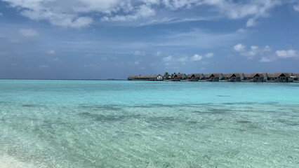 Luxury resort photo of Maldives tropical paradise island in Indian Ocean with overwater thatched bungalows. Beautiful photography, coral reef, azure ocean, sky with clouds. 