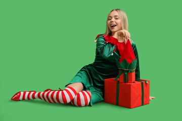 Beautiful young woman in elf costume with Christmas gift boxes on green background