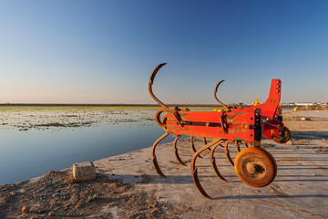 Rusty red plow near flooded rice paddies at sunset in Isla Mayor