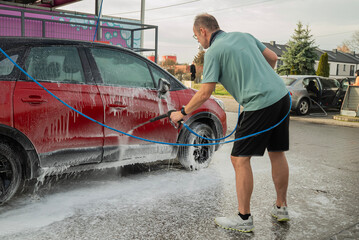 mężczyzna myjący samochód na myjni samoobsługowej