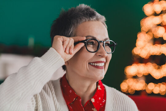 Elderly woman enjoying the festive holiday spirit indoors by a Christmas tree, wearing glasses and a cozy cardigan