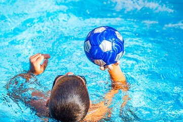 young athletic boy playing ball in the pool