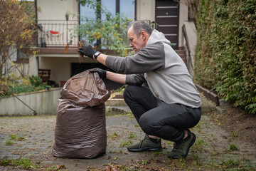 mężczyzna sprzątający opadłe liście do worków wokoło domu © siwyk