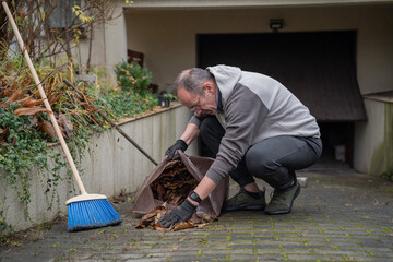 mężczyzna sprzątający opadłe liście do worków wokoło domu © siwyk