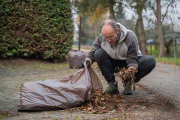mężczyzna sprzątający opadłe liście do worków wokoło domu © siwyk