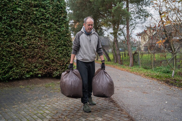 mężczyzna sprzątający opadłe liście do worków wokoło domu © siwyk