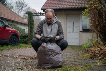 mężczyzna sprzątający opadłe liście do worków wokoło domu © siwyk