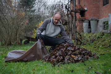 mężczyzna sprzątający opadłe liście do worków wokoło domu © siwyk
