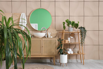 Interior of stylish bathroom with sink, shelving unit, chest of drawers, houseplants and mirror