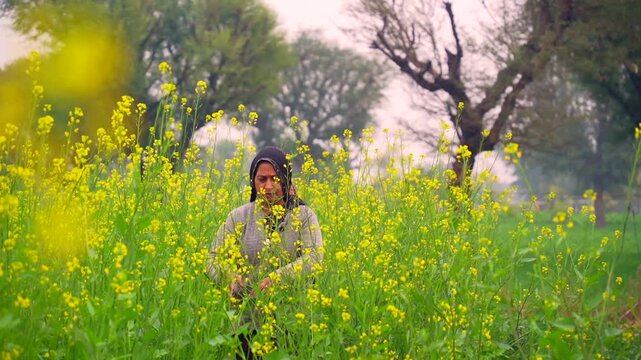 Young woman farmer walking in a mustard field, early morning. Yellow blooming flowers field in village. Lady Inspecting and standing middle of the winter season crops.