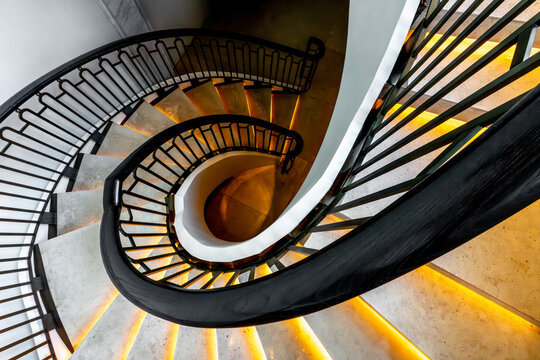 View of a swirling staircase with a dark, wrought-iron railing and glowing steps ascends in a mesmerizing architectural dance, Pathum Wan, Krung Thep Maha Nakhon, Thailand.