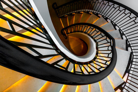 View of a mesmerizing spiral staircase with warm glowing lights accentuating the elegant curves and dark metal railings, Pathum Wan, Krung Thep Maha Nakhon, Thailand.