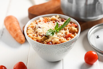 Bowl of pasta fagioli with cheese and basil on white wooden background