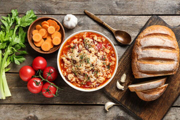 Bowl of pasta fagioli with cheese, bread and ingredients on wooden background