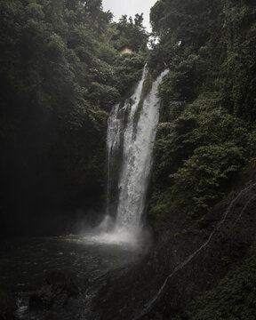 View of cascading waterfalls plunge into a dark pool, surrounded by a dense tangle of lush, vibrant green vegetation, Bali, Bali, Indonesia.