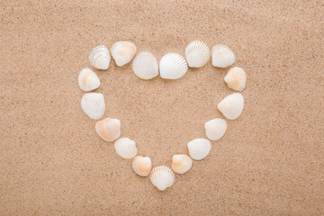 Created heart shape from white sea shells on dry light brown sand background. Closeup. Love concept. Closeup. Top down view.