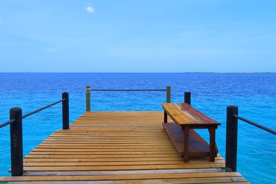 Blue tropical calm ocean, wooden pier with bench. Sunny day on the jetty. Paradise coast under the tropical sky with azure sea.