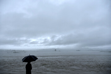 Person with umbrella near a river as dark clouds hover the sky