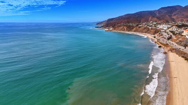 Rocky shore washed by the waters of the Pacific Ocean. Drone footage at the coast of sunny Malibu, California, USA.