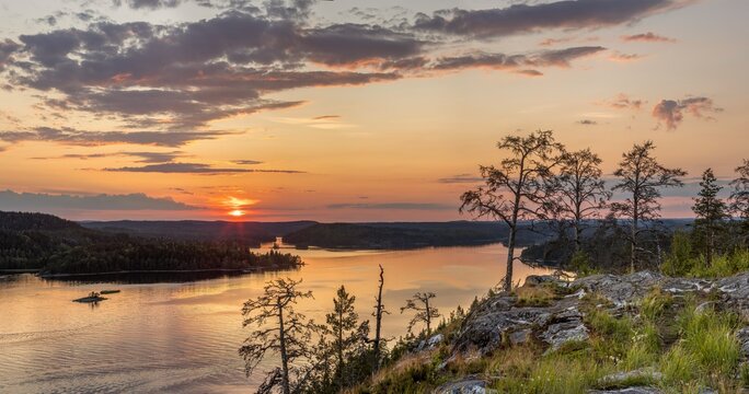 View of the sun dips below the horizon, casting a warm glow over the tranquil lake, its surface reflecting the fiery sky, Sortavala, Russia.