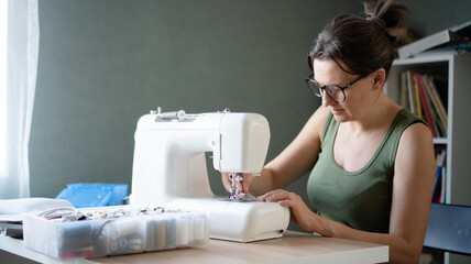 Female tailor using a professional sewing machine to create and assemble a new garment in her bright workshop studio.