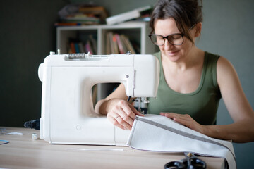 Close up of a pleased and focused female tailor working at her sewing machine, feeling satisfied with her professional sewing project.