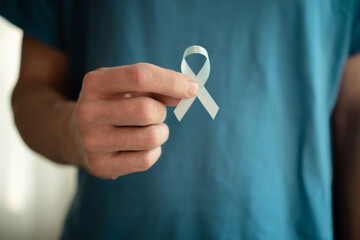 Close up of a man holding a blue satin ribbon in his hand. November awareness month for prostate cancer prevention, early diagnosis, support, and medical treatment concept.