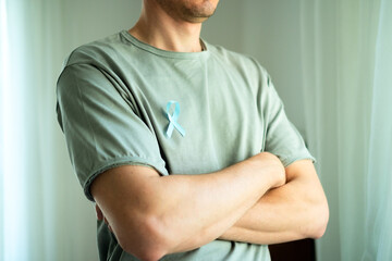 Close up of man with crossed arms and blue satin ribbon on shirt. Symbol of November prostate cancer awareness, early diagnosis, medical help, and support from family and loved ones.